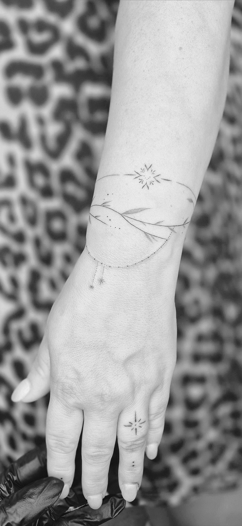 Fineline tattoo: Een armband van blaadjes en sterretjes.