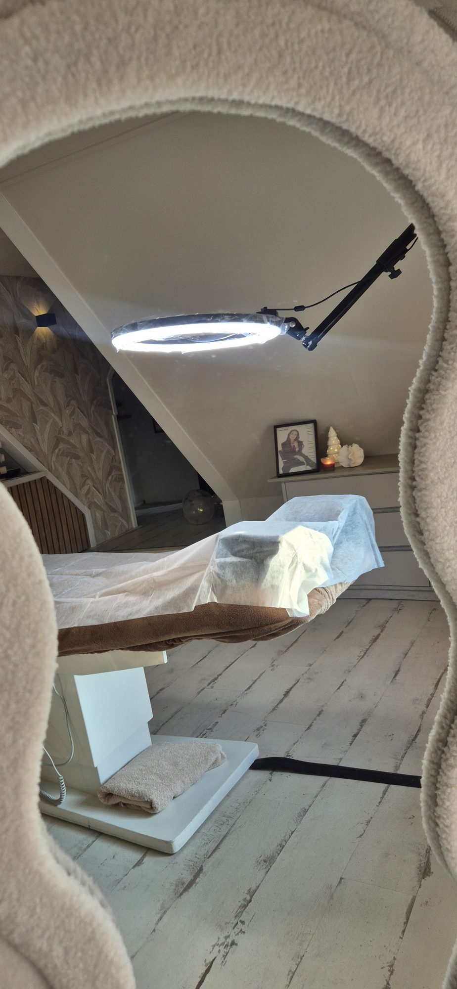 De behandelkamer door de gebogen spiegel: behandelstoel, ringlamp en behang met bladeren