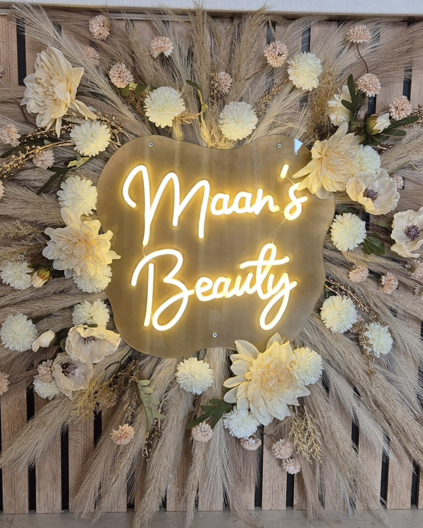 De neon 'Maan's Beauty' op een wand van pampasgras en crèmekleurige bloemen in de salon